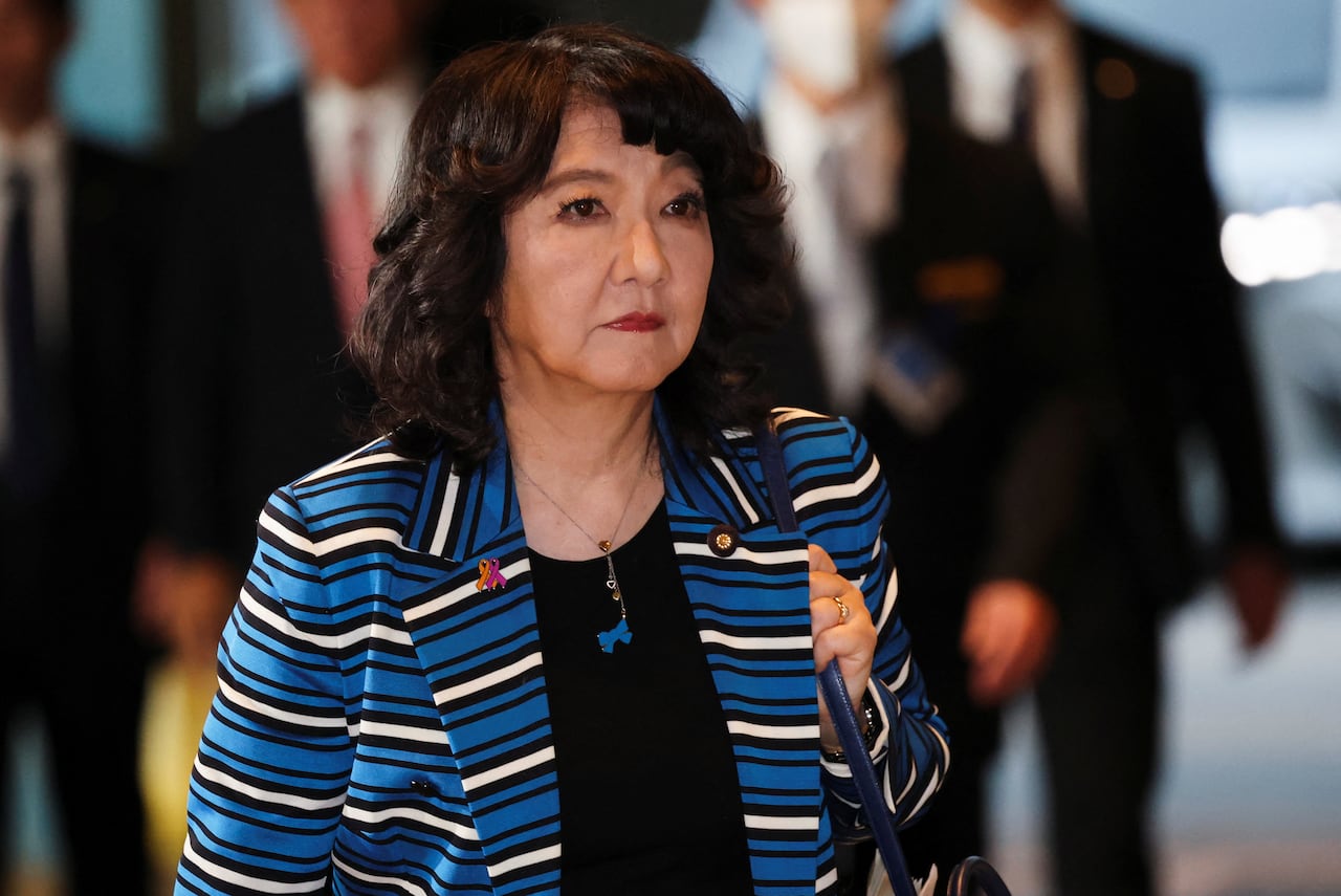 An Asian woman is shown clutching her purse while walking. 