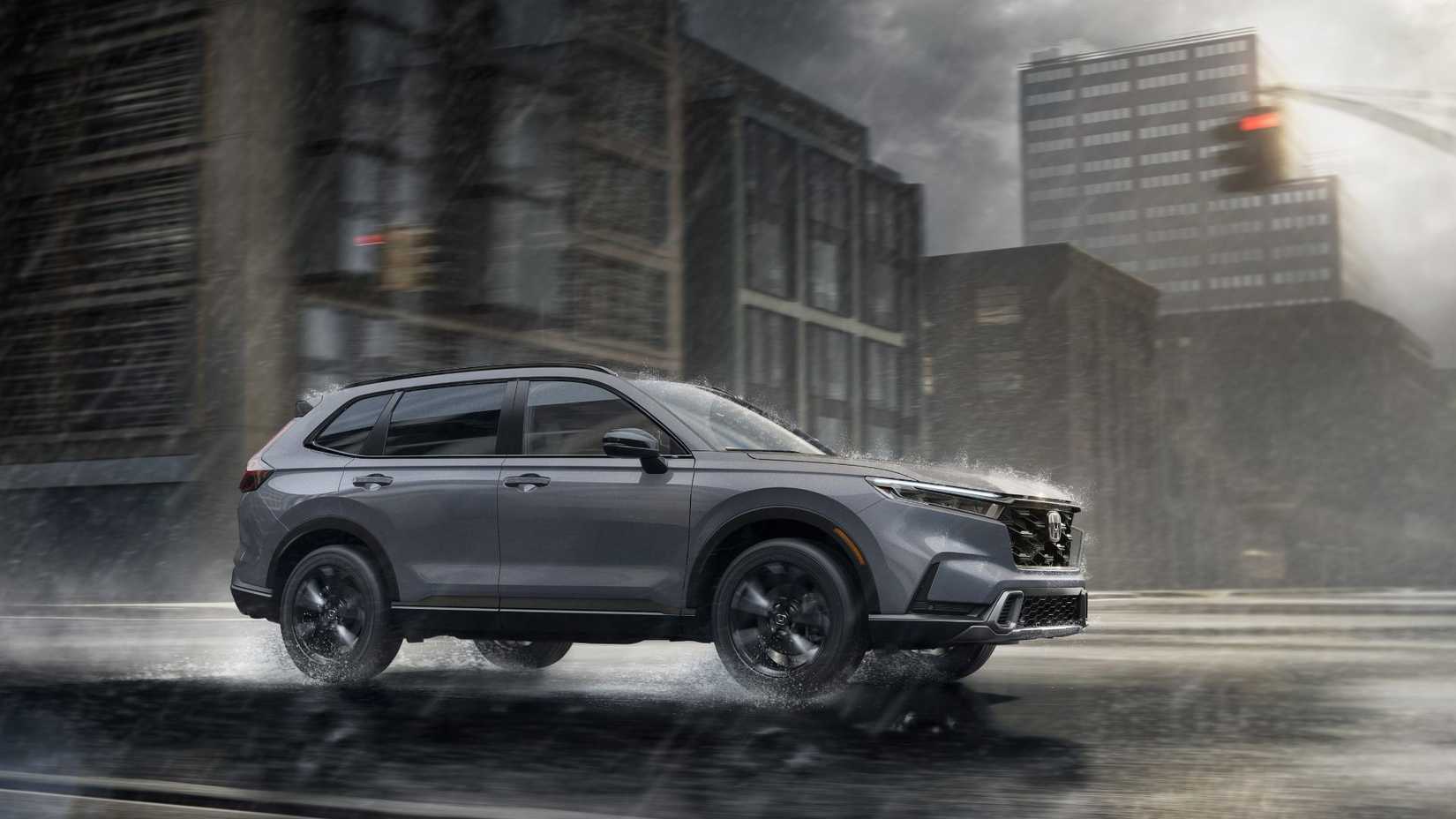 Dynamic front 3/4 shot of a gray 2026 Honda CR-V Sport Touring Hybrid driving in a city in the rain.