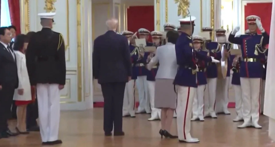 A formal ceremony with dignitaries and military personnel in a grand room, facing a stage or podium