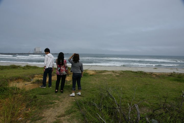Three people stand on grass while looking at the ocean after the tsunami