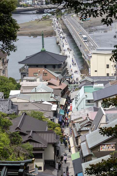 Looking down over Benten Nakamise Street packed with visitors and shops, leading toward the causeway connecting Enoshima Island to the mainland.