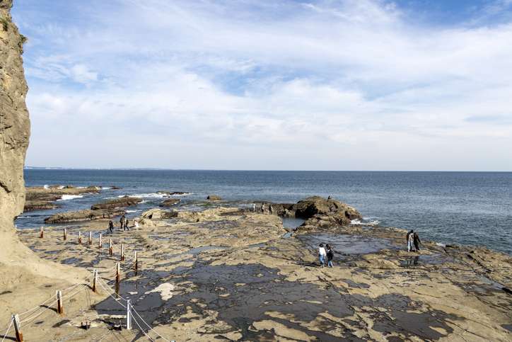 Visitors walking across the tidal rocks at the base of Enoshima’s Iwaya Caves with the Pacific Ocean stretching into the horizon.