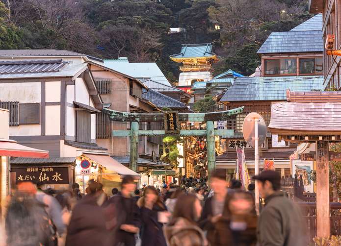 Visitors approaching the bronze torii gate of Enoshima Shrine, leading to the Zuishinmon gate at the end of Benten Nakamise Shopping Street.