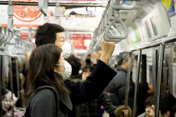 Two asian people wearing face masks to protect from influenza and other respiratory viruses on a crowded train in japan