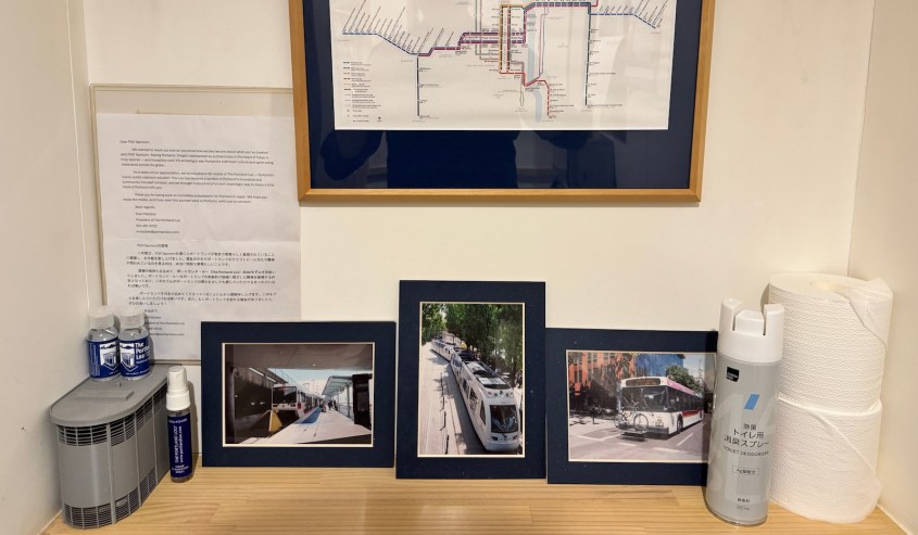 A wooden shelf displaying a map and photos of public transportation, alongside bottles of sanitizer and paper towels.