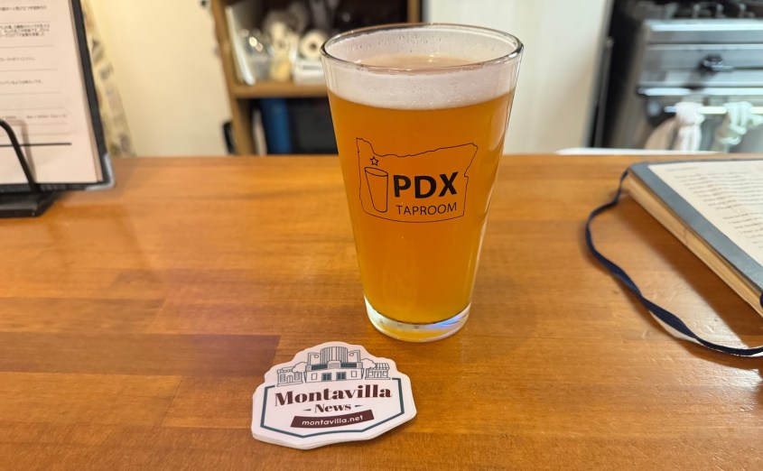 A glass of craft beer from PDX Taproom resting on a wooden bar counter, beside a coaster that reads 'Montavilla News'.