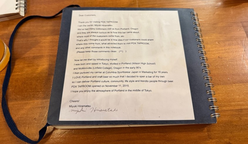 A letter from Miyuki Hiramatsu, owner of PDX Taproom, thanking customers and sharing her background, handwritten in a notebook on a wooden table.