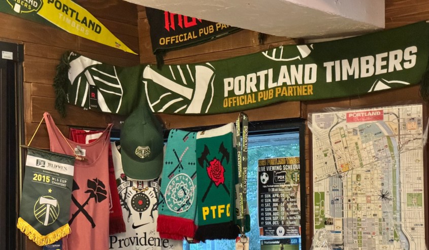 An interior view of PDX Taproom in Tokyo, showcasing Portland Timbers memorabilia including scarves, shirts, and a map of Portland on the wall.