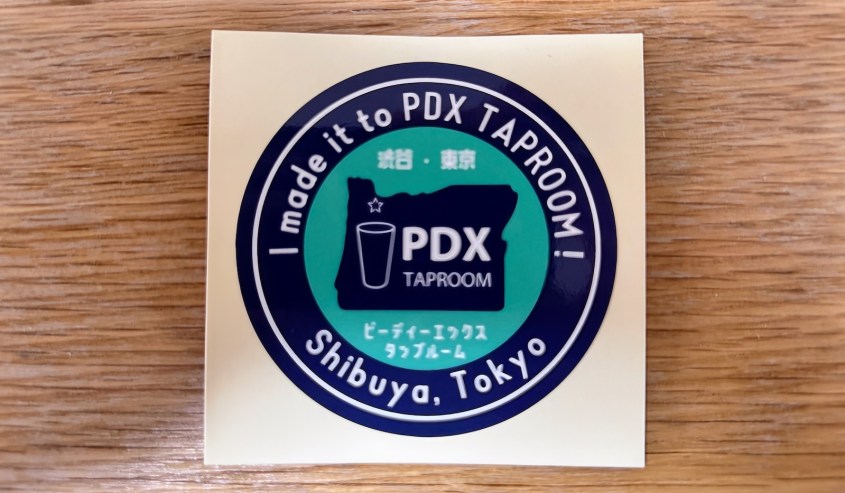 A round sticker with text in both English and Japanese that reads, 'I made it to PDX TAPROOM! Shibuya, Tokyo', featuring an outline of the state of Oregon and a glass.
