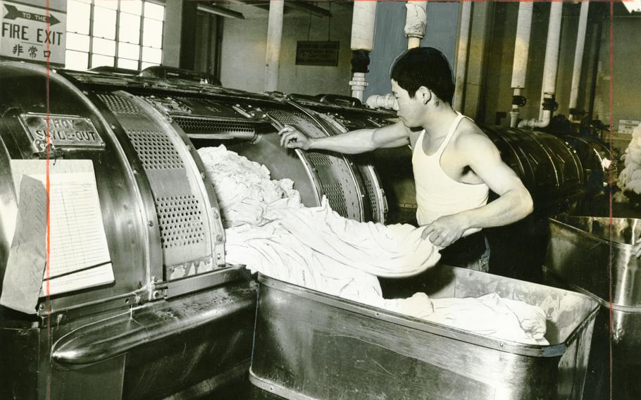 A man in a white undershirt pulls clothes from a machine.