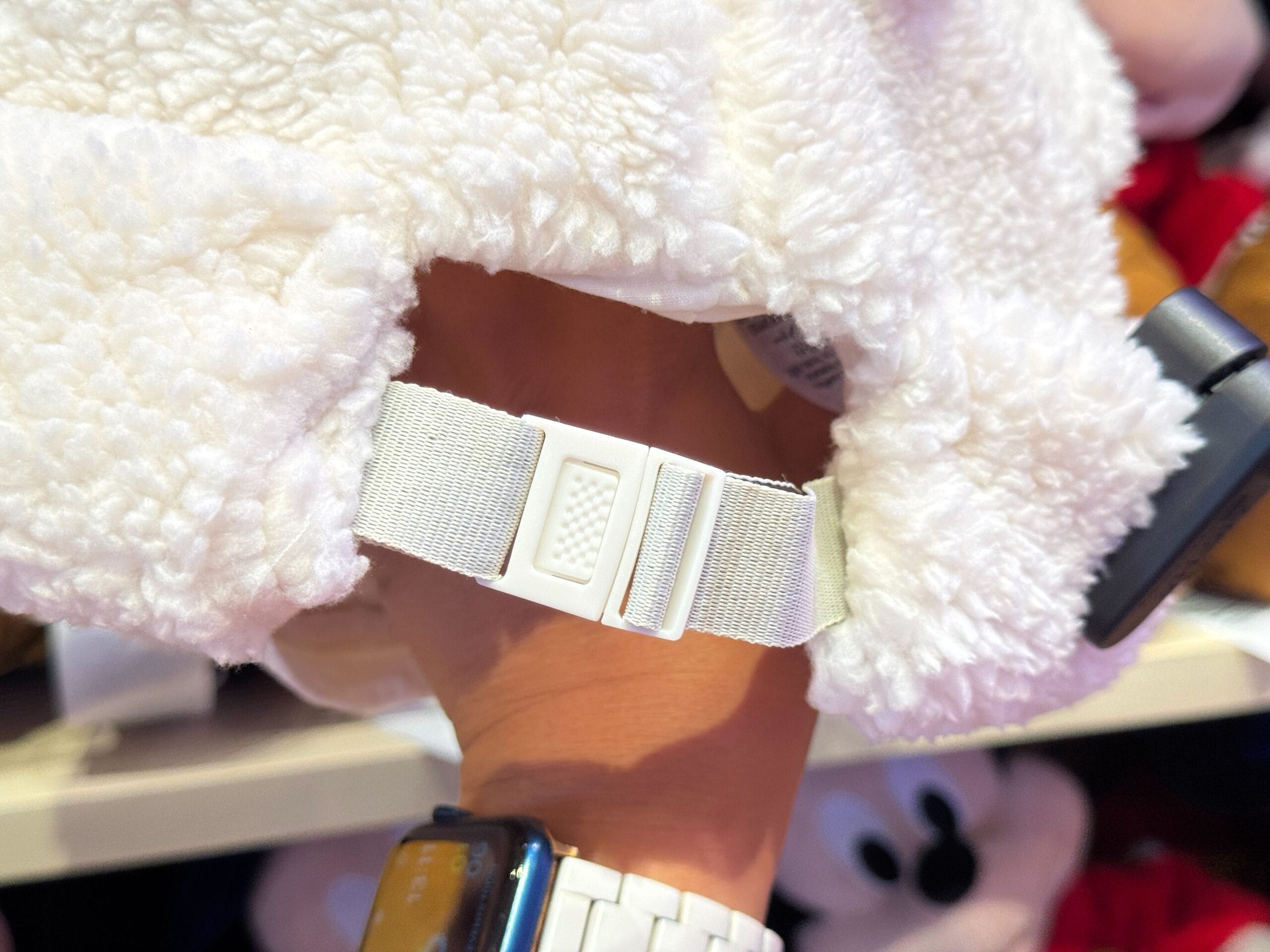 A hand holds a fuzzy white Winter Cap with an adjustable strap, perfect for chilly days at Tokyo Disney Resort.