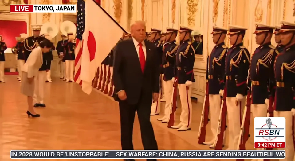 A person in a suit walks past uniformed guards in a formal setting in Tokyo, Japan