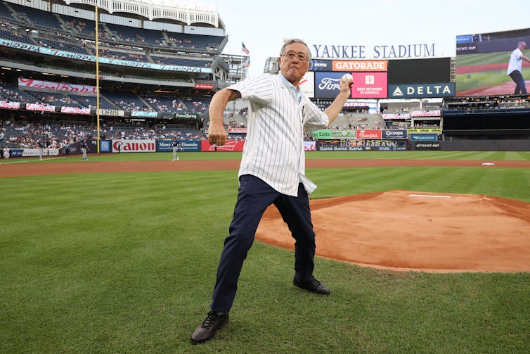 A man in his early 80s wearing Yankees gear gears up to throw a ball at Yankee Stadium.