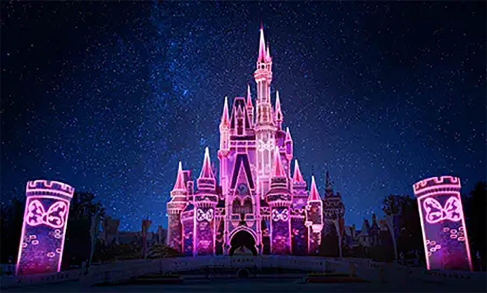 The pink Tokyo Disney Resort castle glows at night, resembling Florida’s Cinderella Castle but with unique spires and colors.