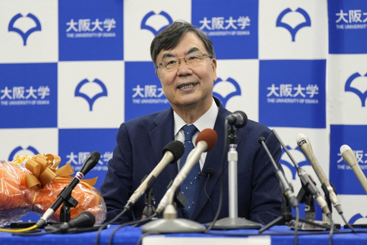 A bespectacled cleanshaven Asian man smiles while speaking from a seated position. He is wearing a suit and tie.