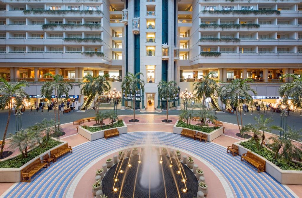 The spacious atrium at Orlando International Airport features palm trees, a central fountain, and multiple floors with balconies. Benches encircle the fountain, offering a serene spot amid the bustling airport vibe where travelers can relax and access convenient COVID-19 testing options.
