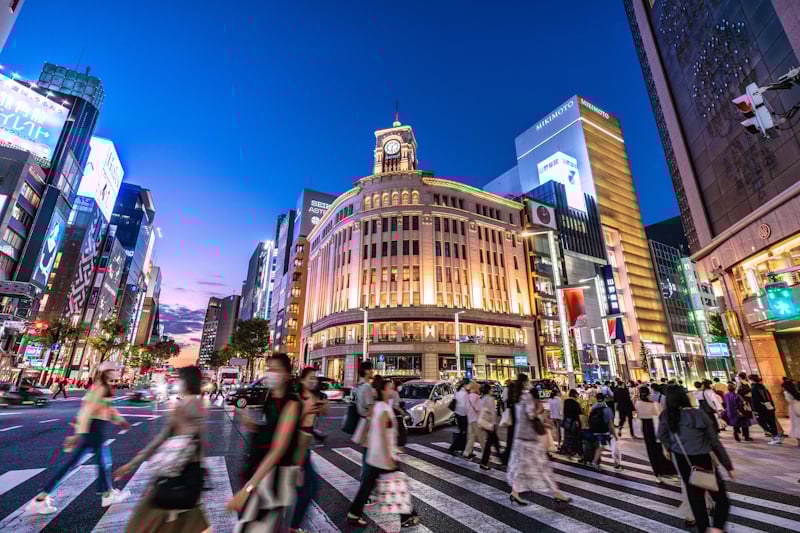 People walking across a crosswalk at Ginza at dusk. 