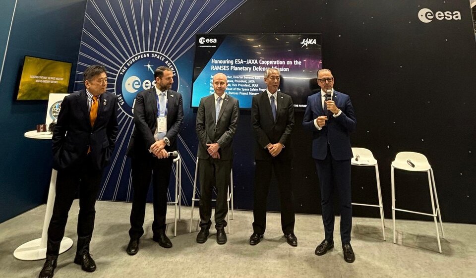 Five men wearing dark suits stand together in front of a dark blue wall with the European Space Agency logo on it