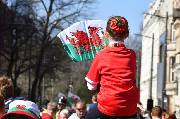Young girl sitting on her father's shoulders waving the Welsh flag