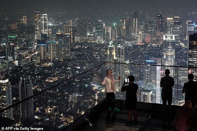 People stand on a transparent-floor deck of an observatory claimed to be Indonesia's highest, at the Thamrin Nine building in Jakarta on July 24, 2025