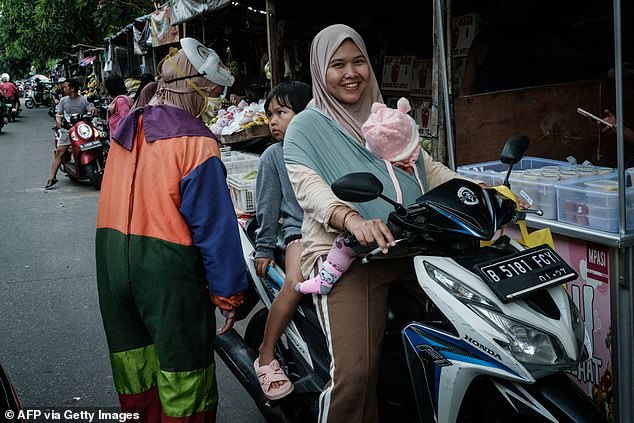 A street performer speaks to a child on a motor scooter in Jakarta on November 8, 2025