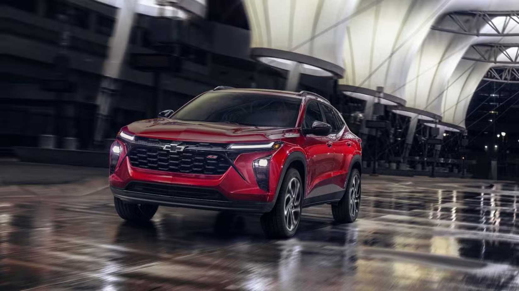 Dynamic fropnt 3/4 shot of a red 2024 Chevrolet Trax RS driving in a city at night.