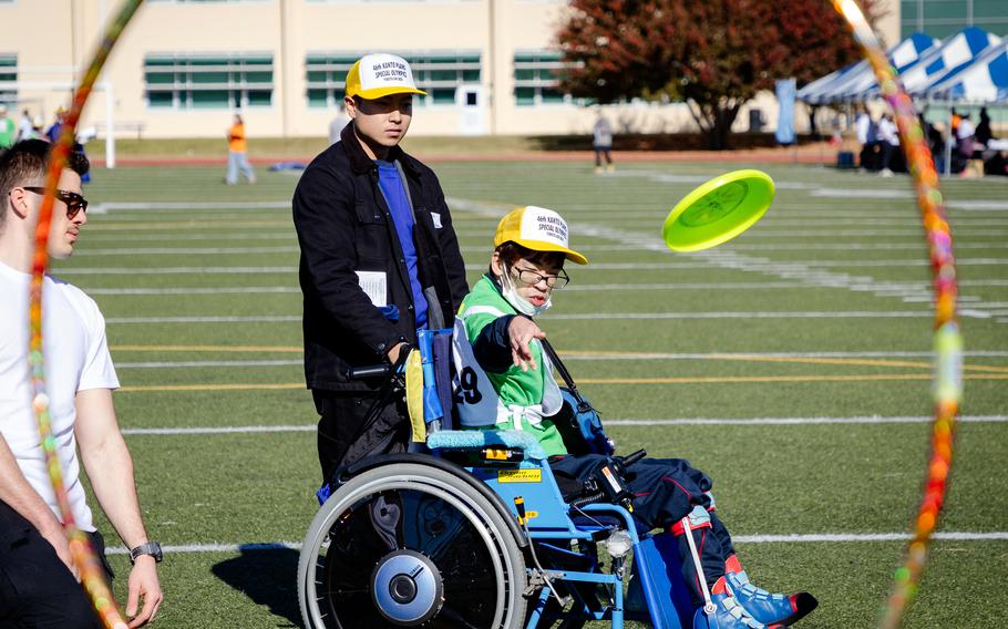 A Japanese athlete seated in a wheelchair tosses a disc on a field.
