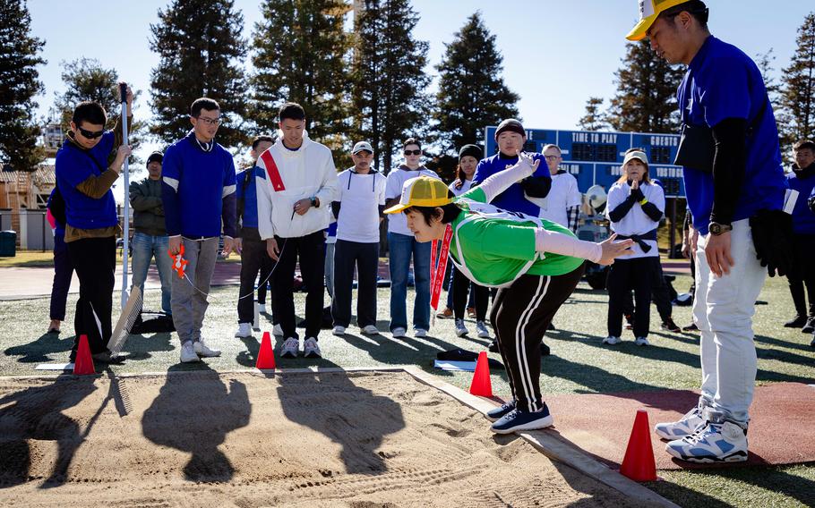 A Japanese athlete prepares to long jump while people cheer.