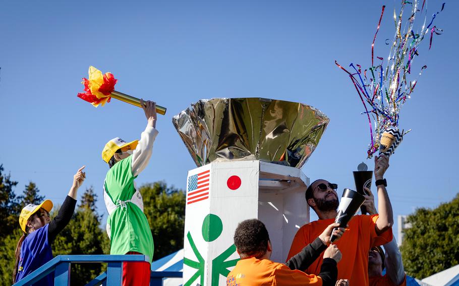 A person holds up a torch made of paper and symbollically lights a large urn while another person throws streamers.