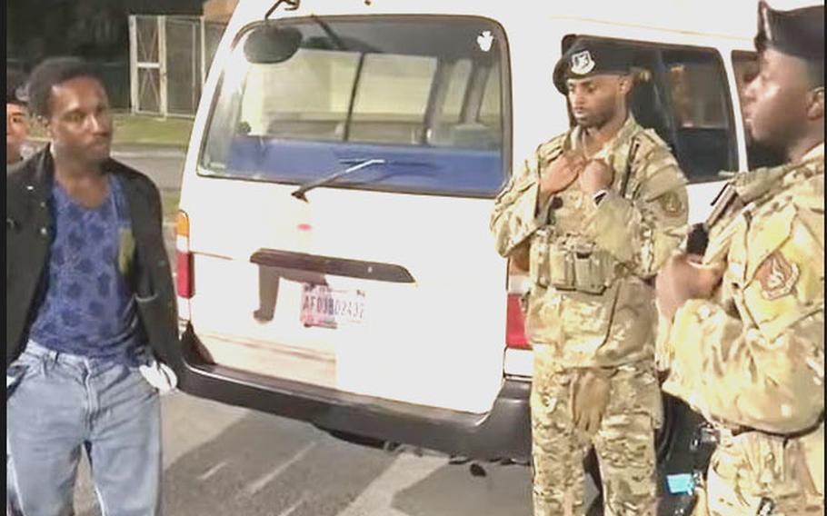 A man talks to military police in front of a white van.