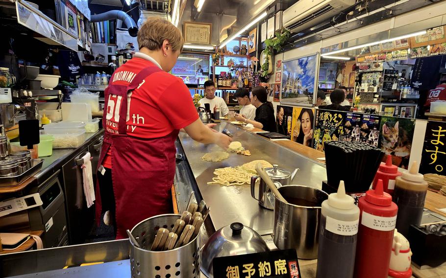 A man stands at a cooking counter in a cluttered market.