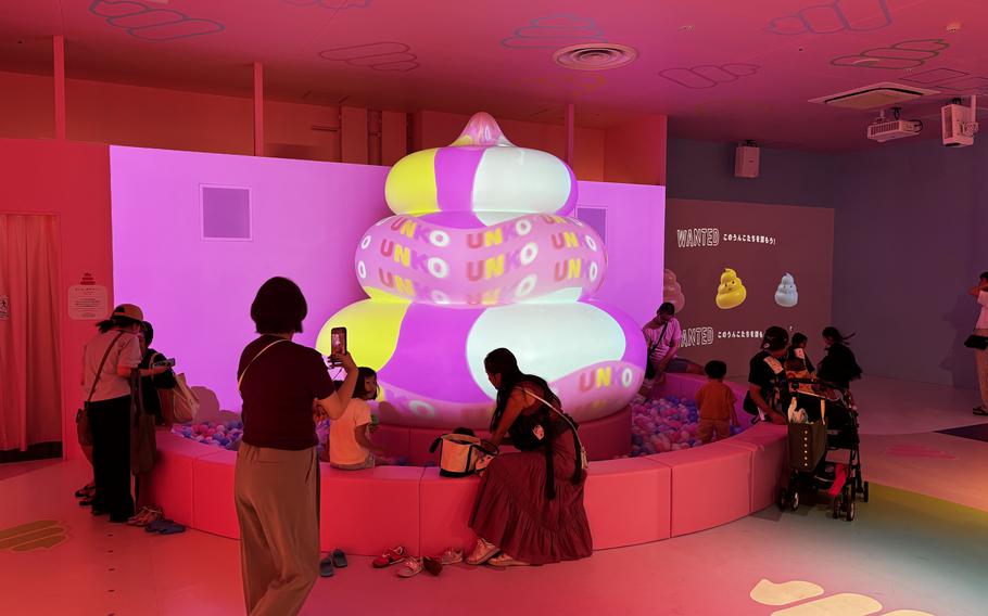 A giant glowing lit-up pile of pink, yellow and white sits in the middle of a room with people around it.
