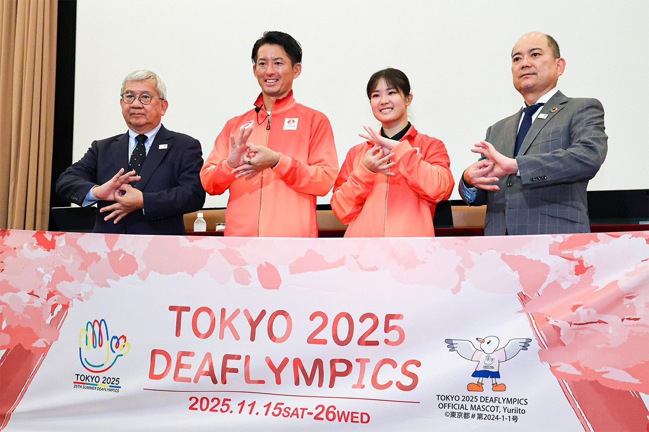 Posing with a gesture used in sign language at an October 2025 press conference for the Tokyo Deaflympics are, from left, Team Japan leader Ōta Yōsuke, men’s soccer team captain and flag bearer Matsumoto Takumi, women’s karate athlete Ogura Ryō, and Ishibashi Daigo, president of the Japanese Federation of the Deaf. (© Jiji)