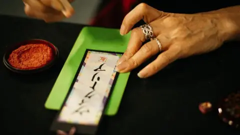 Hyper Japan A display of Japanese lettering on a green background held in place by a woman's left hand.