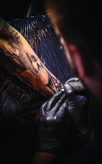 Close up tattoo artist demonstrates the process of getting black tattoo.