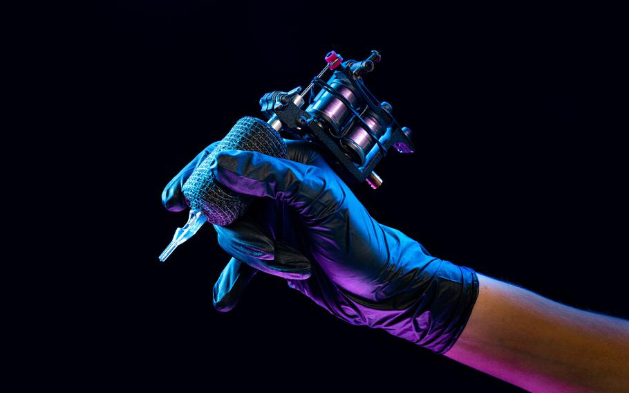 Closeup of tattooer master’s hand in black glove holding machine for making tattoo art on body isolated on dark background in neon. Concept of art, job, hobby, professional equipment. Flyer for ad