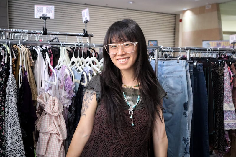 Person smiling in front of clothes
