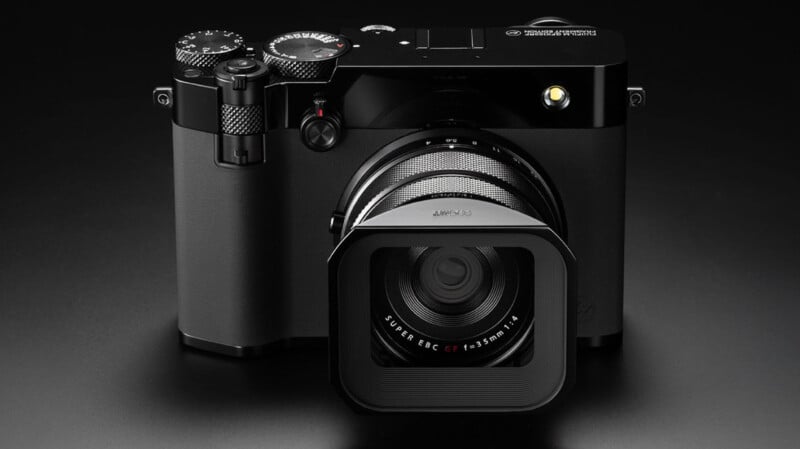 A black digital camera with a square lens hood and detailed control dials is displayed on a dark surface, facing forward.