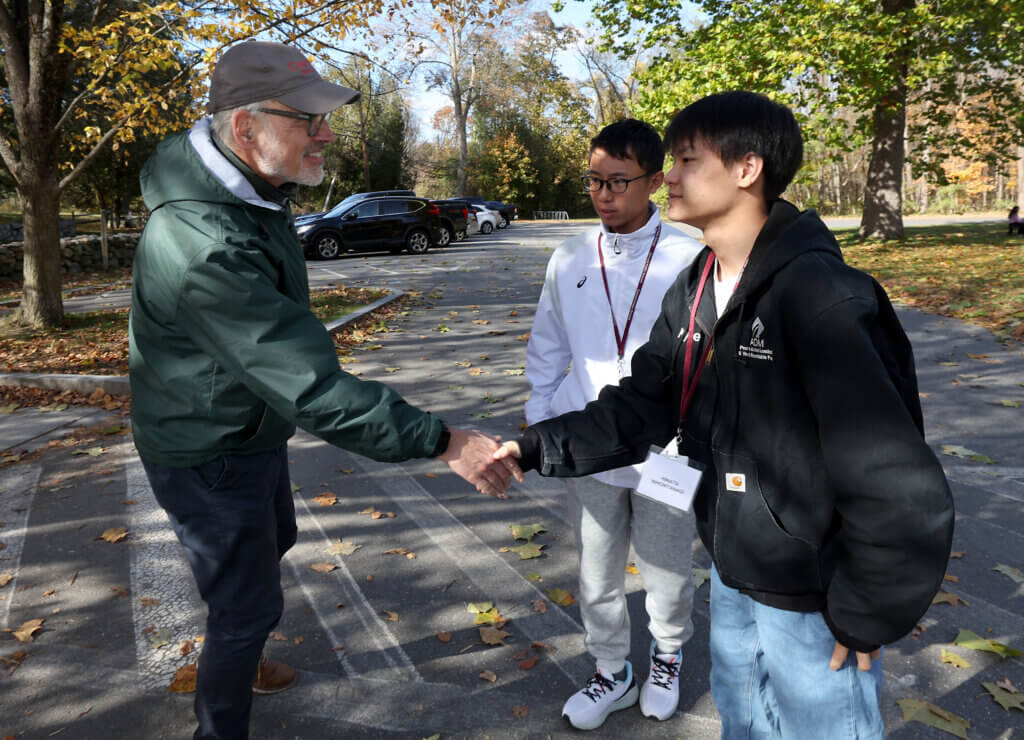 Tour guide Joe Palumbo shakes hands with Nanae student Hinata Nihonyanagi at North Bridge on Tuesday, October 28, 2025. Hinata is one of nine students from Japan visiting Concord this year. Ken McGagh/The Concord Bridge