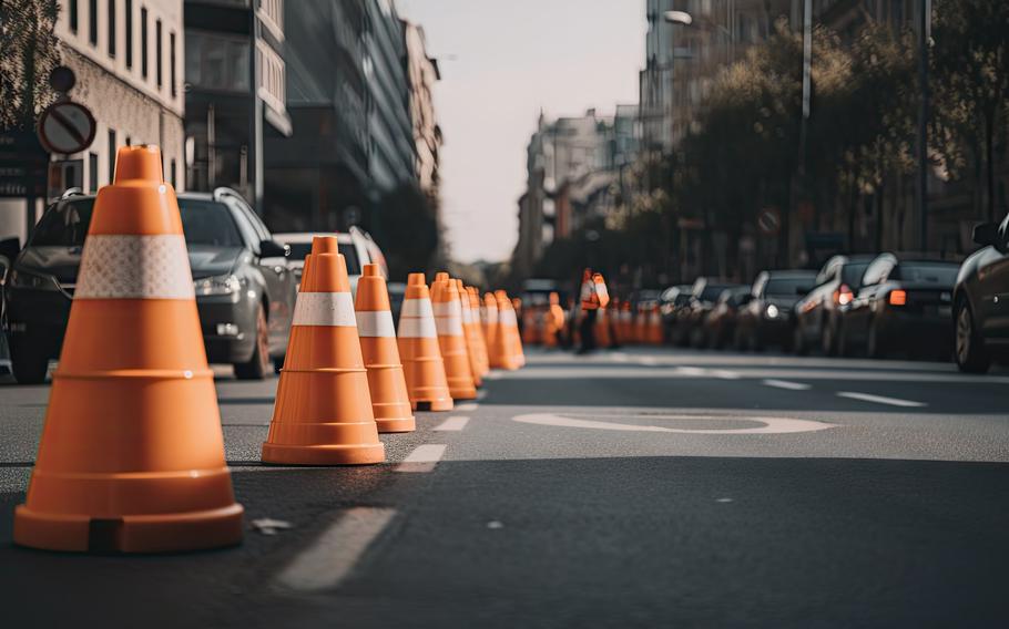 Traffic cones in a row on a busy street with traffic streaming past.