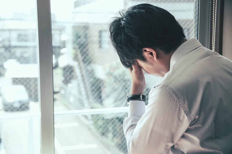Man looking out a window and holding his head as if stressed