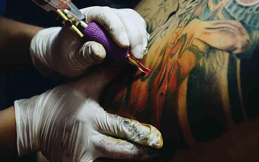 A tattoo artist inking on a customer’s arm.