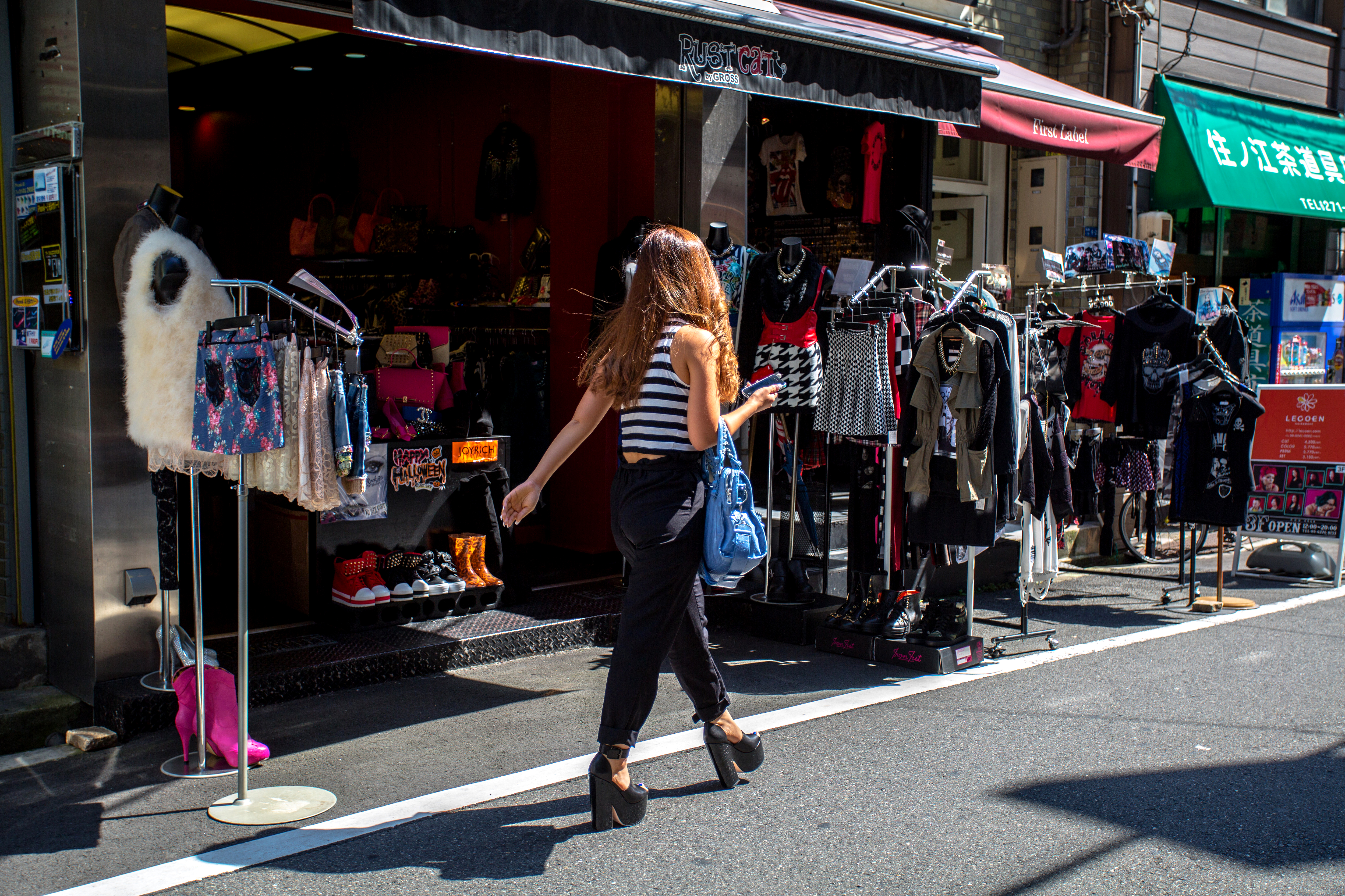 A woman walking past clothing racks in Amerika-Mura, Osaka, Japan
