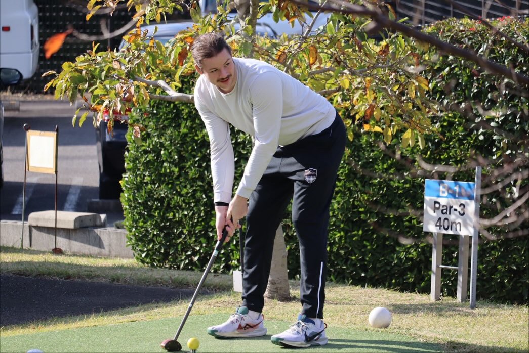 A man playing golf, preparing to hit a yellow golf ball.