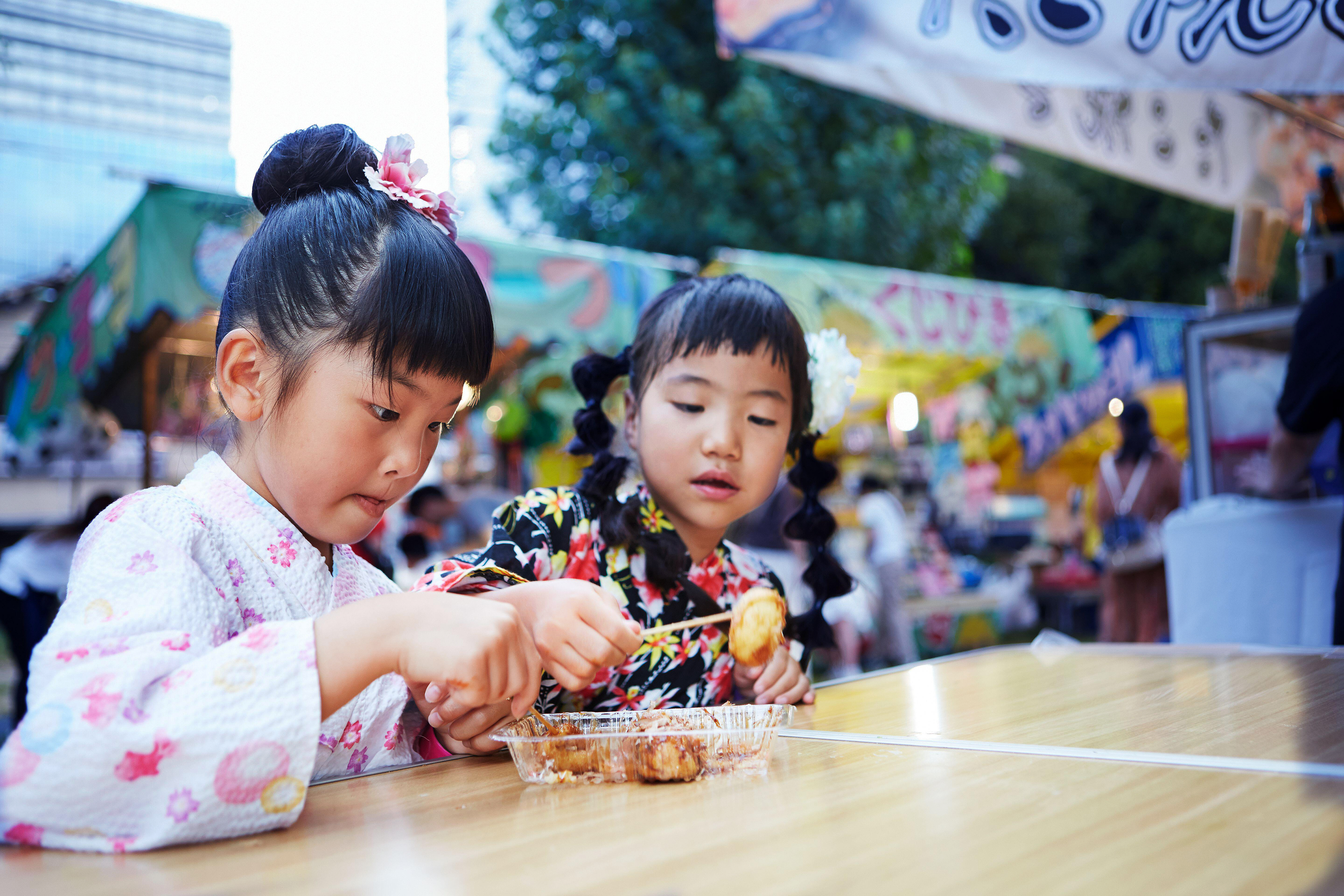Two girls in yukata eating takoyaki in Osaka, Japan