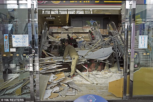 Currently, there is no 'major tsunami warning, tsunami warning or advisory' in place by the JMA. Pictured: A worker cleaning up the aftermath of the earthquake in a broken building