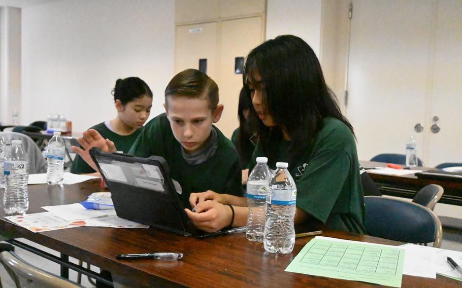 Middle school students seated at a desk work together on a tablet.