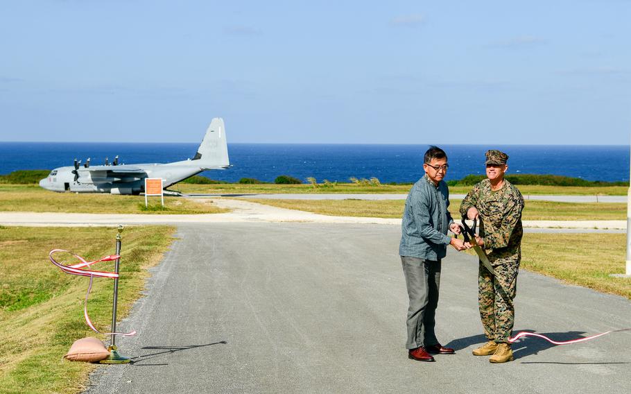 A major general and an Okinawa official hold a giant scissors on the runway of a small island airstrip.
