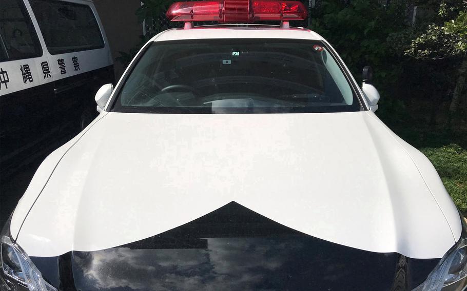 A Japanese police car is parked next to a van.