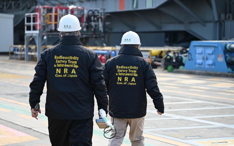 A survey team in white hard hats approaches an aircraft carrier during an exercise.